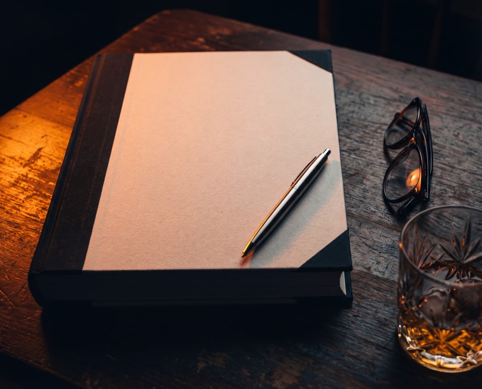 A bound document on a dark wooden table with a pen and reading glasses.